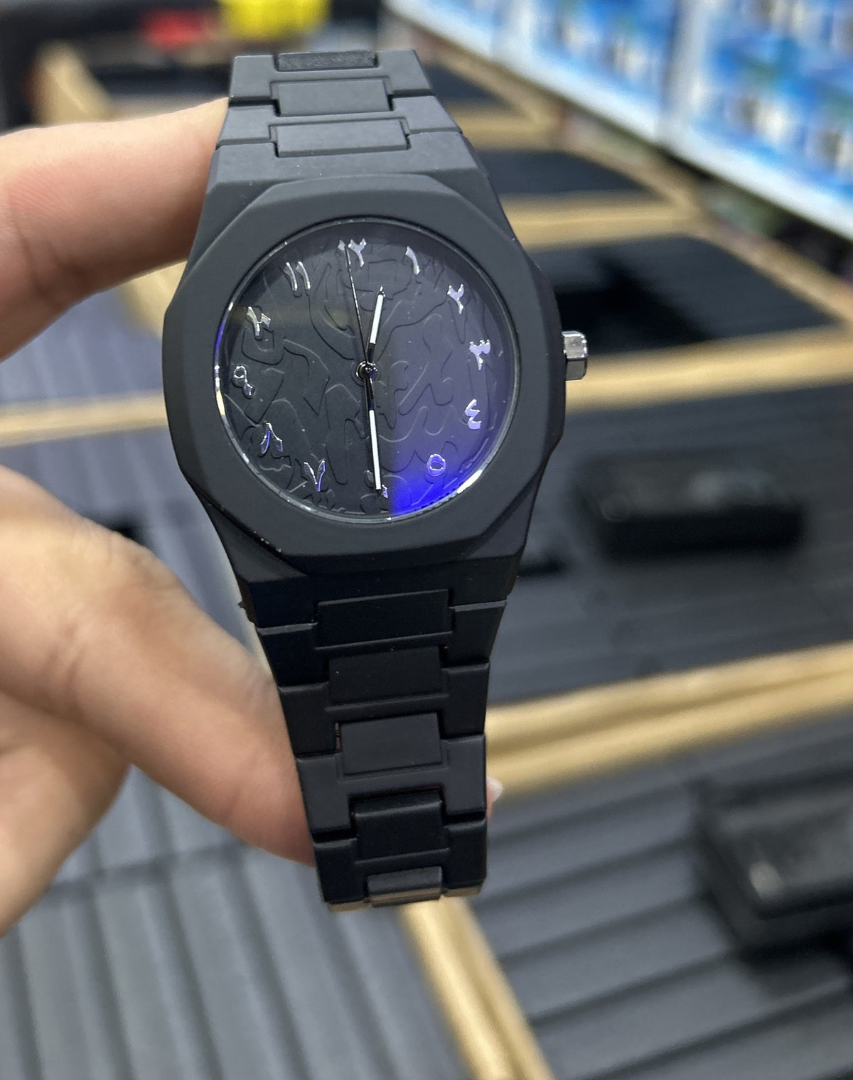 Reloj negro mate de policarbonato con números arábigos plateados sobre esfera texturizada, sostenido en la mano (foto real)