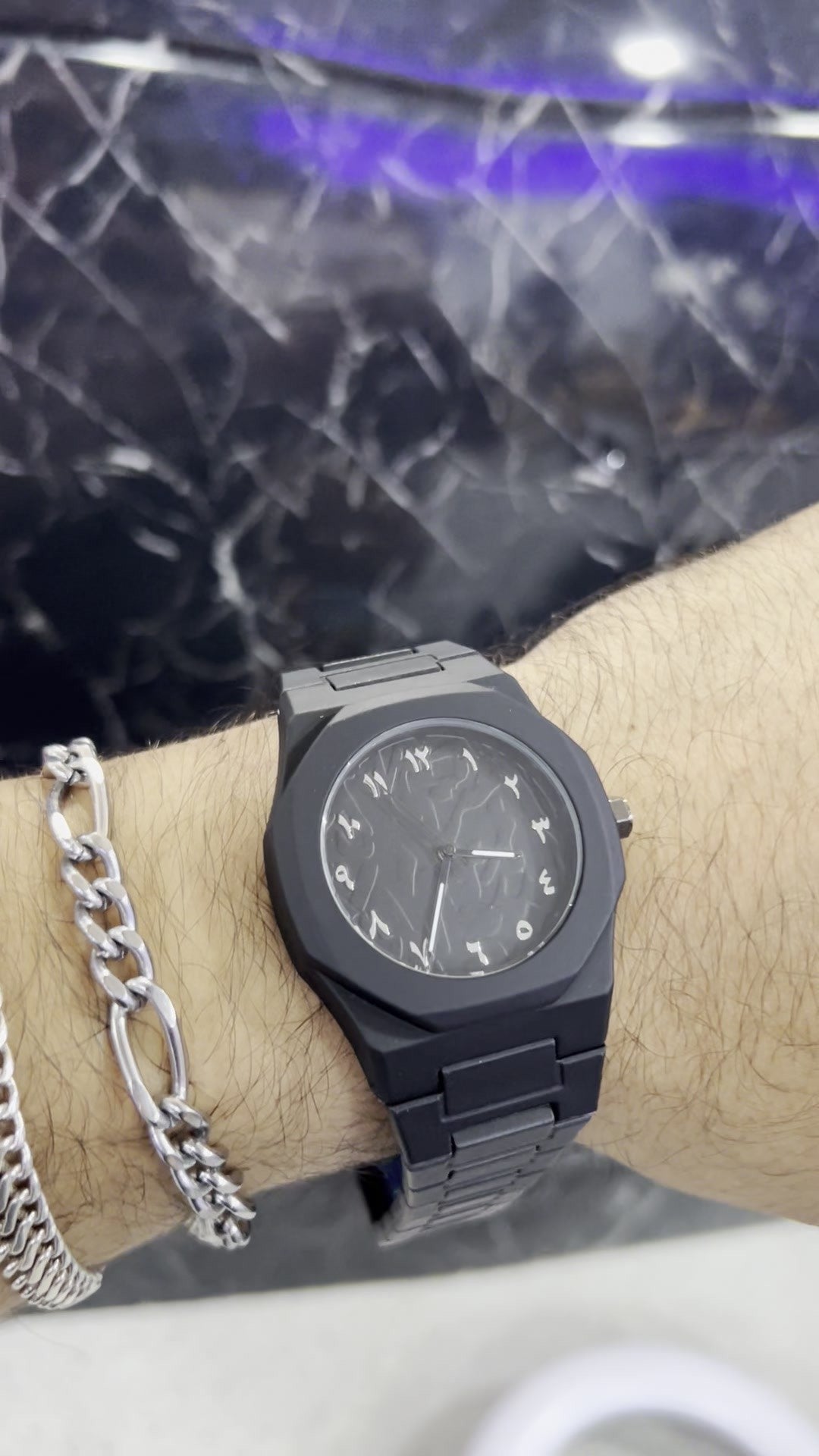 Reloj negro mate de policarbonato con números arábigos plateados puesto en la muñeca (foto real)