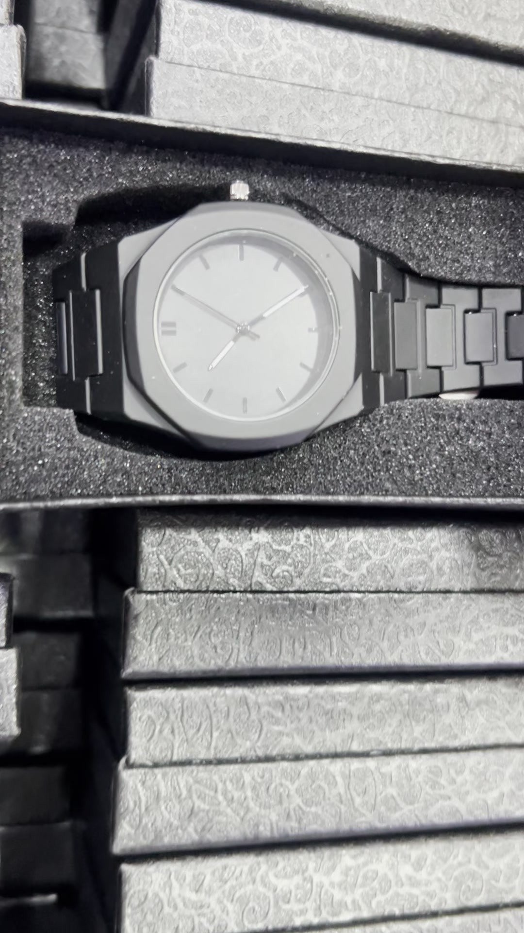 Reloj negro mate de policarbonato liso con esfera gris e índices de barra, dentro de su caja (foto real)