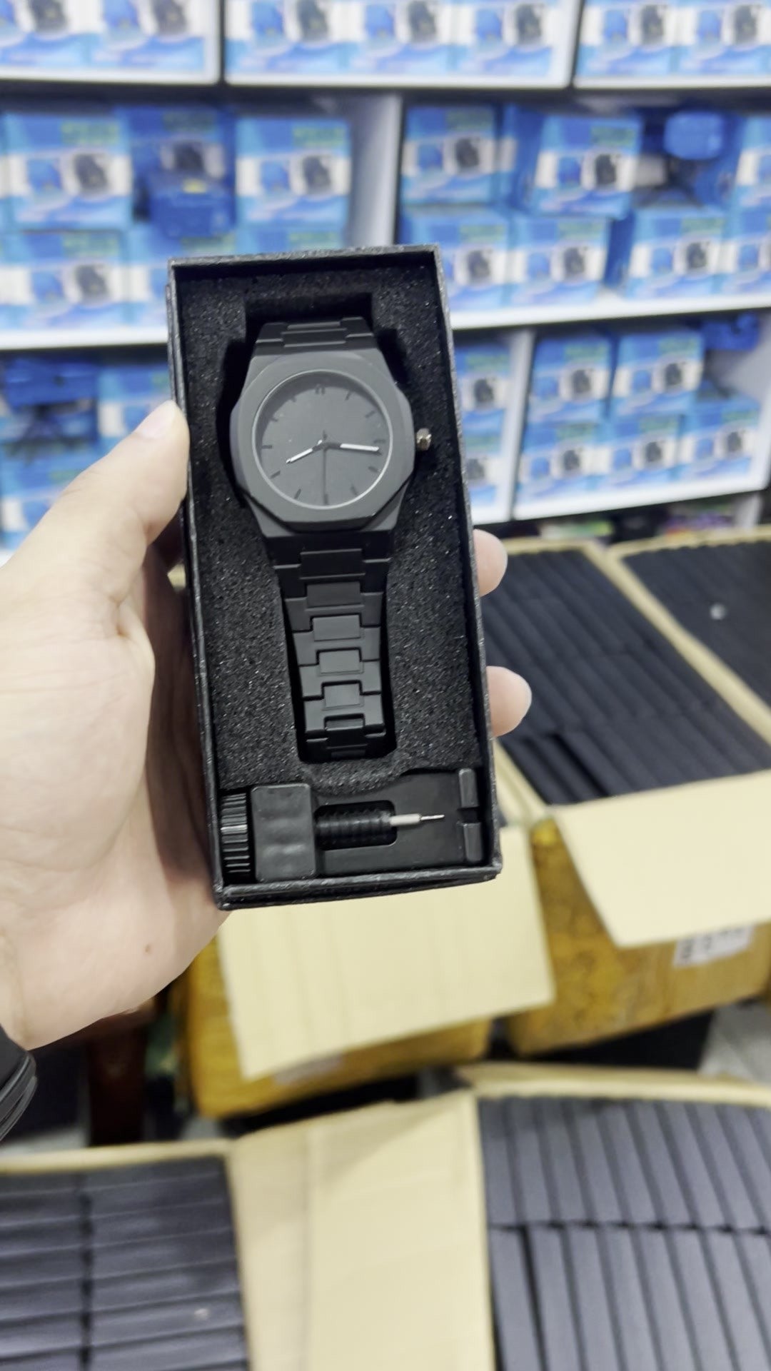 Caja de regalo con el reloj negro mate liso y la herramienta, sostenida en la mano (foto real)