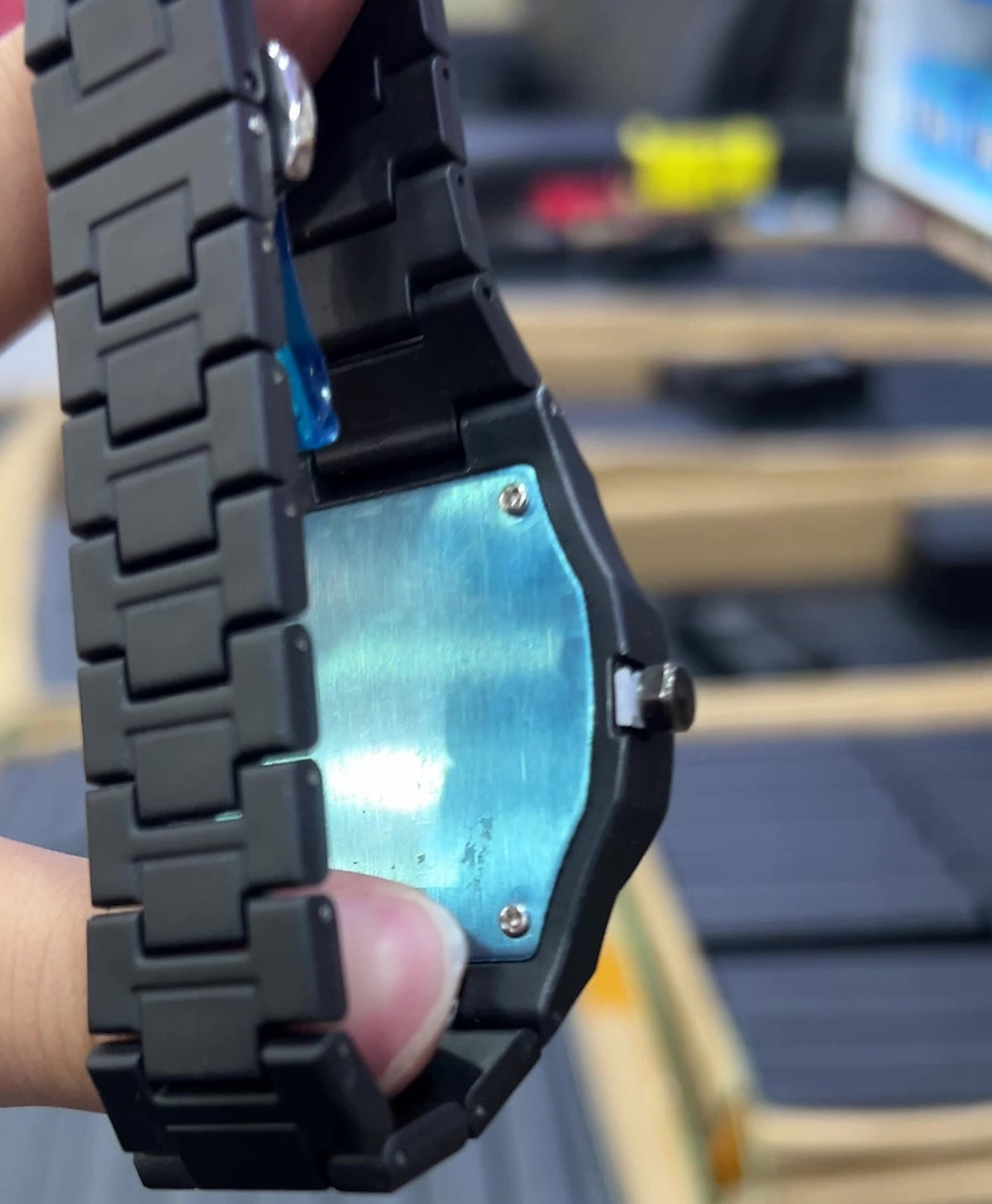 Reverso del reloj negro mate: placa metálica con 4 tornillos y película protectora azul que se retira al estrenarlo; igual en ambos modelos (foto real)